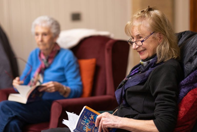 Due persone anziane su una poltrona leggono un libro sorridenti